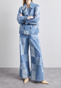 Denim jacket and wide-leg pants in varying shades of blue, featuring a patchwork design. Smooth texture with double-breasted front and large collar.