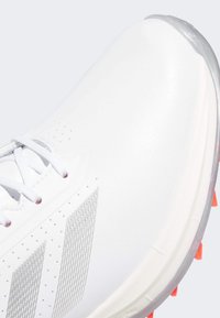 Witte sportieve sneaker met een gladde synthetische bovenkant, zilveren accenten en perforaties voor ventilatie. De zool heeft feloranje noppen.
