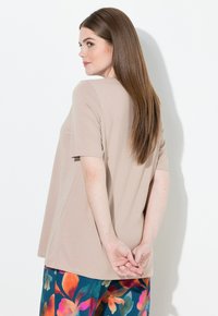 Beigen värinen lyhythihainen toppi, jossa rento istuvuus ja pyöreä kaula-aukko, yhdistetty värikkäisiin kukkakuosisiin housuihin. Sileä pinta, yksinkertainen muotoilu.