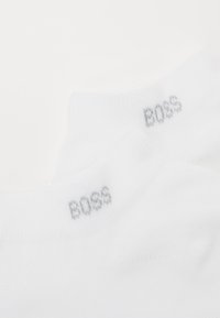 Fehér zoknik bordázott szegéllyel, az "BOSS" márkanevével világosszürkében a bokánál. Simma textúra, minimál dizájn.
