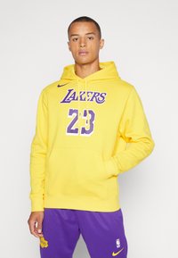 Moletom amarelo com logótipo roxo dos "Lakers" e o número 23, apresentando um bolso frontal, capuz com cordão e punhos canelados. Combinado com calças roxas.
