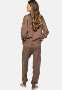 Ensemble de détente en tricot marron comprenant un pull à coupe décontractée et un pantalon fuselé avec des poignets et une taille côtelés. Texture douce et couleur chaleureuse.