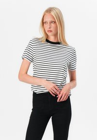 Black and white striped t-shirt with short sleeves and a black crew neckline. Worn with high-waisted black jeans, featuring a fitted design.