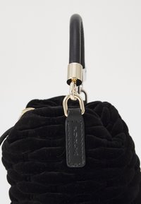 Sac à main en velours noir avec un design texturé et froncé. Il dispose d'une poignée en cuir noir, de quincaillerie dorée et d'une étiquette portant le mot "PURLA" en relief.
