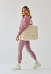 Różowa bluza noszona z jasnoróżowymi legginsami. Beżowa torba na ramię z napisem "READY SET GLOW". Białe sneakersy z pastelowymi akcentami.