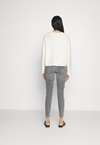 Suéter blanco de corte relajado, combinado con jeans ajustados grises. El suéter tiene un escote redondeado y una textura suave. Calzado negro.