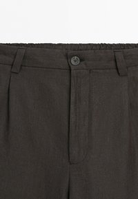 Pantaloni su misura grigio scuro con vita, passanti per cintura, chiusura con bottone e dettaglio elastico sul retro.