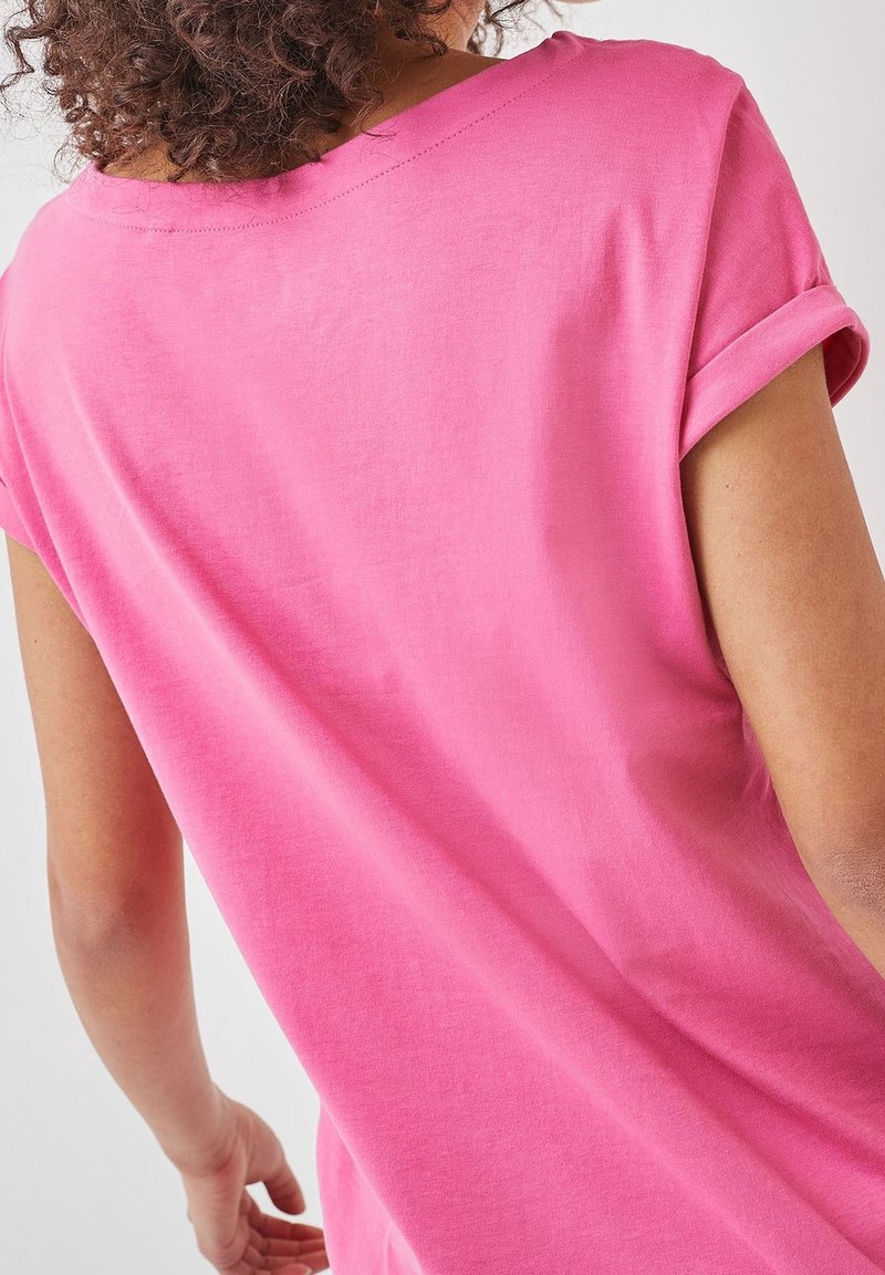 Camiseta de algodón rosa con un corte relajado, mangas enrolladas y un escote amplio, con textura suave y mínimos detalles de costura.
