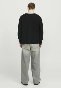 Sort struktureret sweater med en hvidstribet krave, parret med lysegrå brede bukser. Looket er afslappet og moderne.