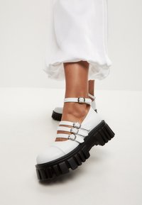 Scarpe platform bianche con più cinturini fissati da fibbie di metallo argentato, caratterizzate da una suola in gomma nera spessa e una finitura liscia.