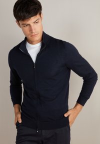 Granatowy sweter zapinany na zamek, wykonany z delikatnej przędzy, posiada stójkę, długie rękawy oraz ściągacze przy mankietach i na dole.
