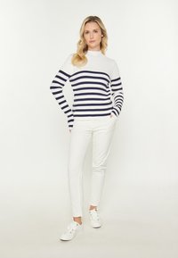 Pulover alb cu dungi orizontale bleumarin, guler înalt, asortat cu pantaloni albi slim și adidași albi. Design simplu și modern.