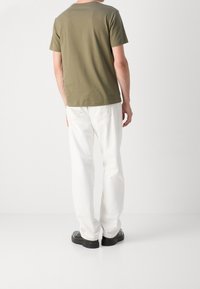 Olivgrön bomullst-shirt med rund hals, bärs med vita byxor med raka ben och svarta skor, fotograferad bakifrån.