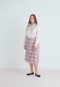 Svetlo béžová košeľa s gombíkmi, vzorovaná midi sukňa v pastelovom dizajne so zigzag vzorom a čierne ploché topánky. Hladká tkanina, pohodlný strih a sukňa po kolená.