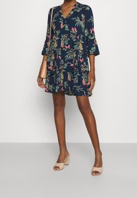 Blommönstrad klänning i marinblått med trekvartslång ärm och v-ringning. Har en lager-på-lager design med flerfärgade blomblad och blad.