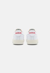 Ténis brancos de couro com uma sola creme texturizada. Logotipo vermelho "Reebok" no calcanhar e forro interior azul. Design clássico de cano baixo.
