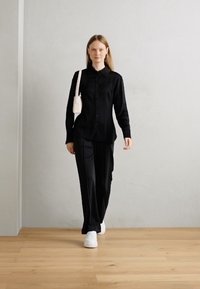 Chemise noire à boutons et pantalon assorti, associés à des baskets plateformes blanches. Un petit sac blanc est porté en travers de l'épaule.