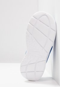 Modrá sportovní bota s texturovanou bílou gumovou podrážkou, s otiskem loga. Bota má hladký, měkký povrch a zakřivený design.