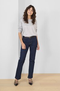 Sivi pulover, modri traperji, črni sandali s peto na naramnice. Traperji so ravno krojeni, z klasičnim pet-imetrovnim dizajnom. Gladke teksture.