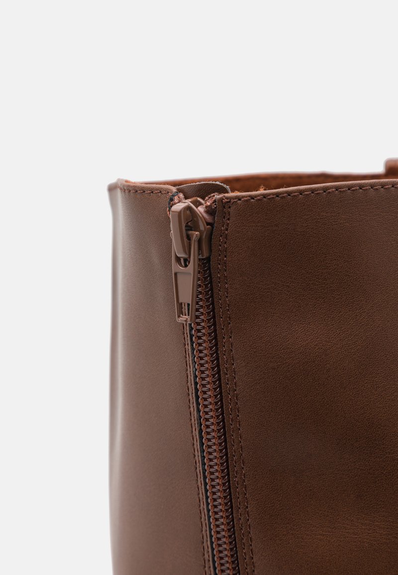 Braune Lederstiefel mit seitlichem Reißverschluss, glatter Textur und verstärkter Naht entlang der Kanten. Kompakte, abgerundete Knöchellinie.