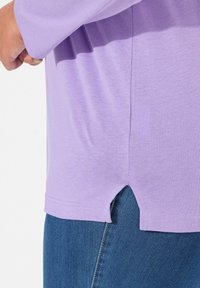 Hellblaues T-Shirt mit geradem Schnitt, hat einen leichten Schlitz am Saum. Der Stoff wirkt weich, mit glatter Textur. Kombiniert mit blauen Jeans.