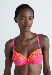 Roze en oranje geprikte onderwire beha met doorschijnende cups, bloemenpatronen, verstelbare bandjes en decoratieve strikjes op de bandjes.