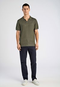 Olivgrön kortärmad polotröja med krage, i kombination med mörkblåbyxor och vita sneakers. Enkel stickad struktur och avslappnad passform.