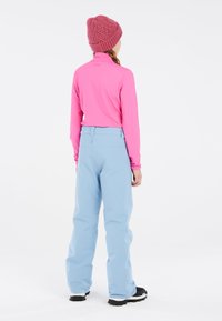 Camiseta rosa de manga larga con cuello alto, combinada con pantalones de nieve azul claro. El atuendo se complementa con un gorro texturizado rosa y botas negras.