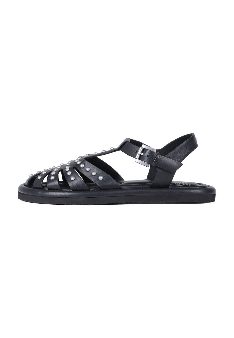 Sandalias de cuero negro con un diseño abierto, que cuentan con adornos de tachuelas y una correa ajustable en el tobillo para un ajuste seguro. Suela de goma.
