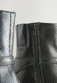 Czarne botki za kostk�ę z faux skórki z teksturowanym wzorem w wąż, z boku z zamkiem błyskawicznym oraz elastycznymi akcentami umożliwiającymi dopasowanie.