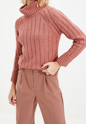 Pull col roulé rose avec texture côtelée et détails en tricot torsadé sur les épaules, assorti à un pantalon matchant.