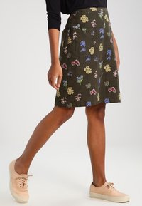 Falda de patrón floral en verde oscuro con flores amarillas, rosas y azules. Corte en A, de longitud hasta la rodilla, confeccionada en tejido texturizado.