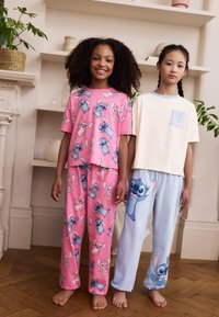 Zwei Mädchen tragen passende Schlafanzüge. Das erste Set ist rosa mit Comicfiguren. Das zweite Set ist hellblau mit einem Muster auf der Hose.