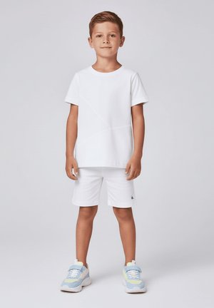 Biała koszulka z krótkim rękawem i pasujące szorty. Tkanina wydaje się gładka, z subtelnymi liniami wzoru. Obuwie z niebieskimi, żółtymi i białymi akcentami.