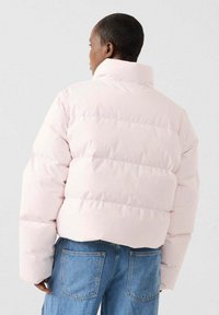 Opgeblazen jack in lichtroze, met horizontale gestikte secties, een hoge kraag en brede mouwen, gecombineerd met lichtblauwe spijkerbroeken.