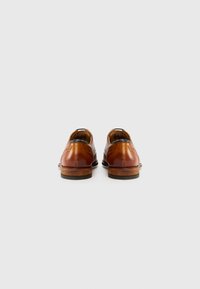 Zapatos de cuero marrón con una textura suave, punta redondeada y detalles de costura mínimos. Tacón de madera con una base oscura contrastante.