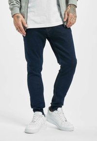 Slim-fit tummansiniset farkut, valmistettu puuvillasekoitteesta, jossa on hienovarainen pinta. Yhdistetty valkoisiin tennareihin kontrastiksi.