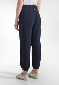 Granatowe, lekkie spodnie dresowe o zwężanych nogawkach, z elastycznym pasem, ściągaczami przy kostkach i gładką fakturą. Zestawione z jasnymi butami.