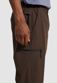 Bruine cargobroek met een elastische tailleband, zijzakken en een ritszak met zwarte ritsdetails. Soepele, duurzame stof.