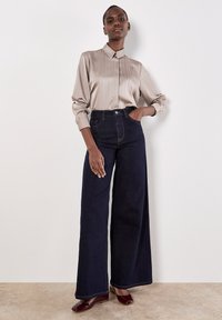 Blusa di raso beige chiaro con righe verticali e colletto abbinata a jeans a gamba larga blu scuro, con vita alta e hardware minimale.