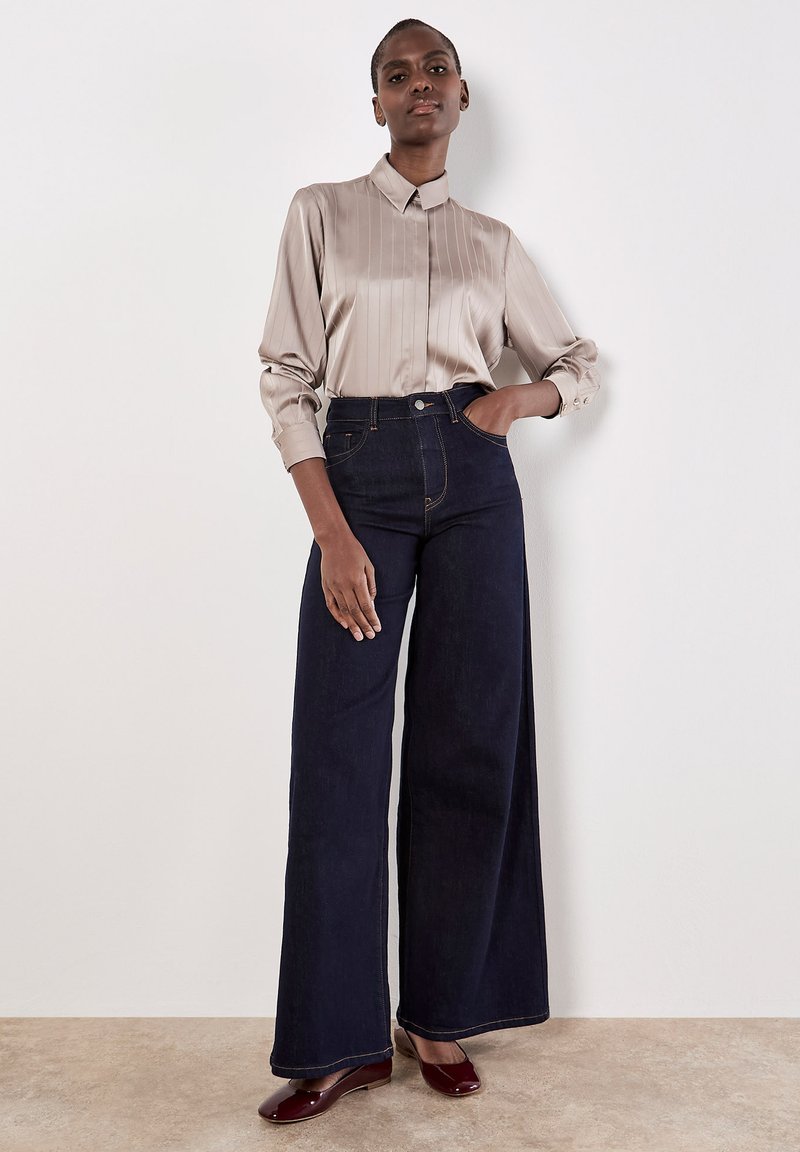 Blusa di raso beige chiaro con righe verticali e colletto abbinata a jeans a gamba larga blu scuro, con vita alta e hardware minimale.
