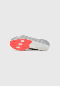Gray and white athletic shoe sole with a textured surface. Bright red accents on the heel and strategic cutouts for enhanced grip.