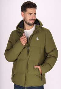 Giacca isolante verde oliva con cappuccio, foderata in nero, chiusura frontale con zip e tasche laterali. Presenta un piccolo logo sul petto.