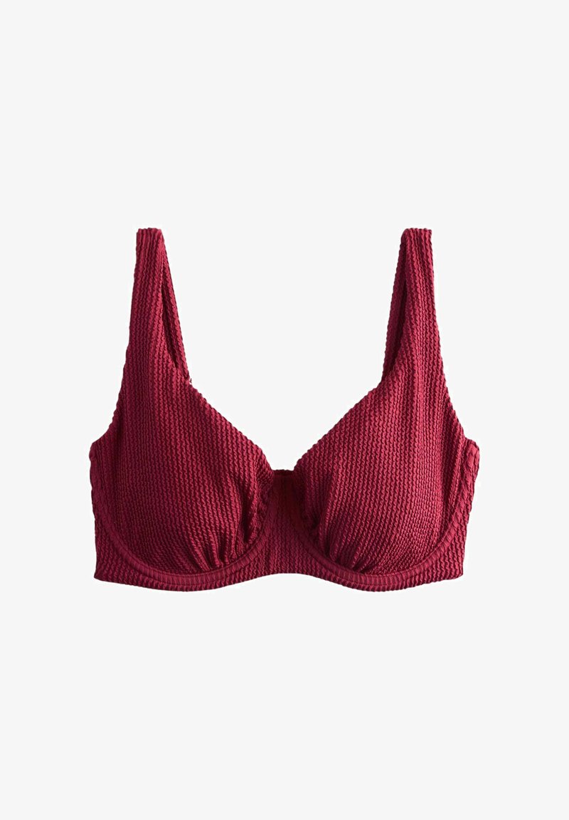 Sarkanas teksturētas auduma krūšturis ar stīpu atbalstu un platām plecu siksnām, attēlots uz balta fona.