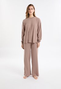 Luźny zestaw do noszenia w domu z żebrowanej tkaniny w miękkim beżowym kolorze, z długimi rękawami i spodniami o szerokich nogawkach, wykonany z teksturowanej tkaniny.