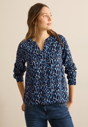 Marineblauw blouse met een blauw-witte abstracte luipaardprint, lange mouwen en een ingesneden halslijn. Draag met donkere jeans.