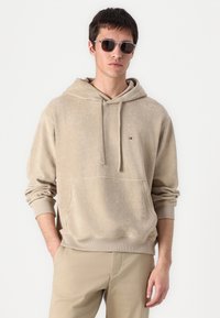 Hanorac bej cu glugă, fabricat din fleece moale, cu buzunar tip kangaroo, manșete ribbate și un logo mic pe piept.