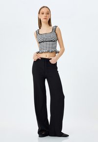 Zwarte geribbelde brede broek gecombineerd met een zwart-witte geblokte crop top met knoopjes aan de randen en een vierkante halslijn.