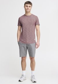 Rød melert t-skjorte med korte ermer og rund hals, kombinert med lysegrå kne-lange shorts og hvite joggesko.