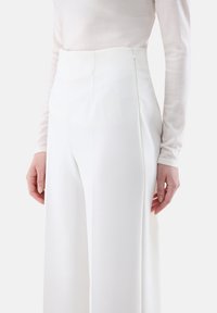 Weiße hochgeschnittene Hosen aus einem glatten Stoff mit geradem Schnitt, seitlichen Taschen und einem verdeckten Reißverschluss im Rücken.